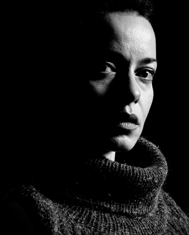 Black and white image of an actor portrayal of Trudhesa patient looking forward with face in shadow and turtle-neck sweater